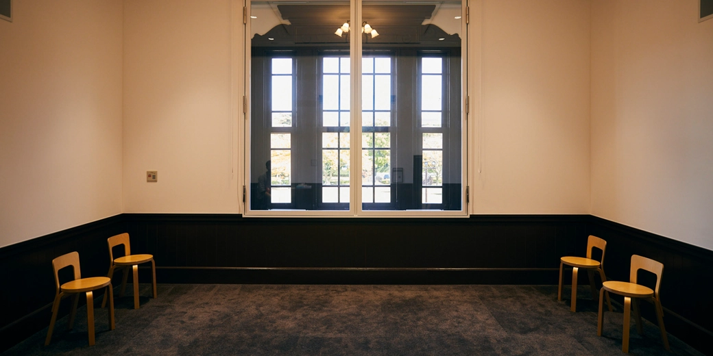 Photo : In a room with a large window in the middle, there are two wooden chairs lined up on each side.