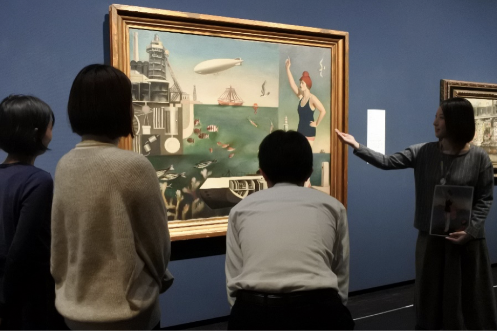 絵画の前で四人の男女が話しながら鑑賞している写真。