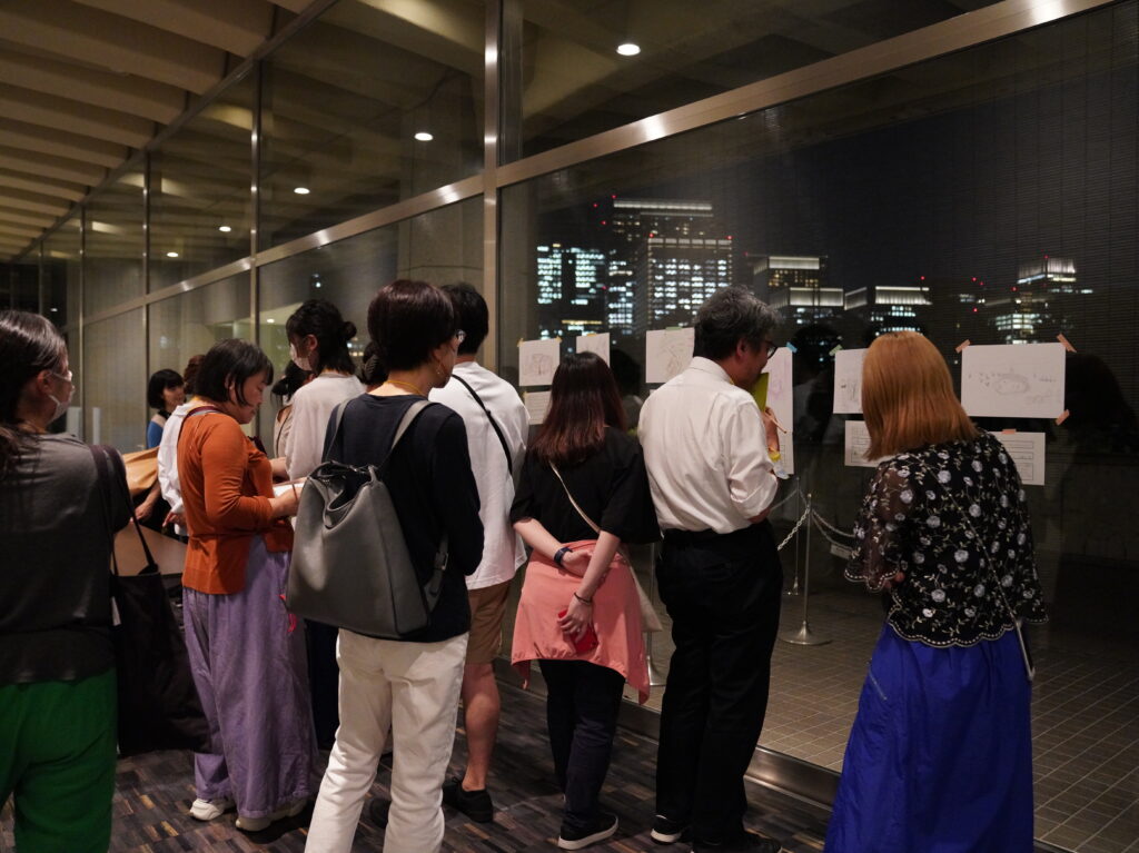 窓越しに夜景が見える。窓ガラスに模写した絵を貼って、多くの人が眺めている。
