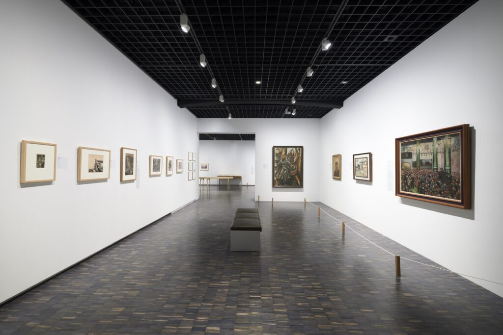 白壁の展示室。真ん中にはベンチ。右壁には油彩画。左壁には版画が展示されている。